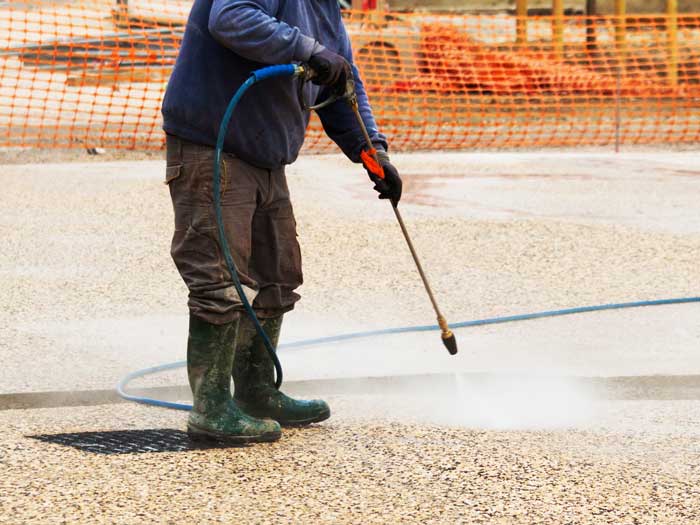 Ouvrier qui nettoie à l'eau haute pression du béton désactivé